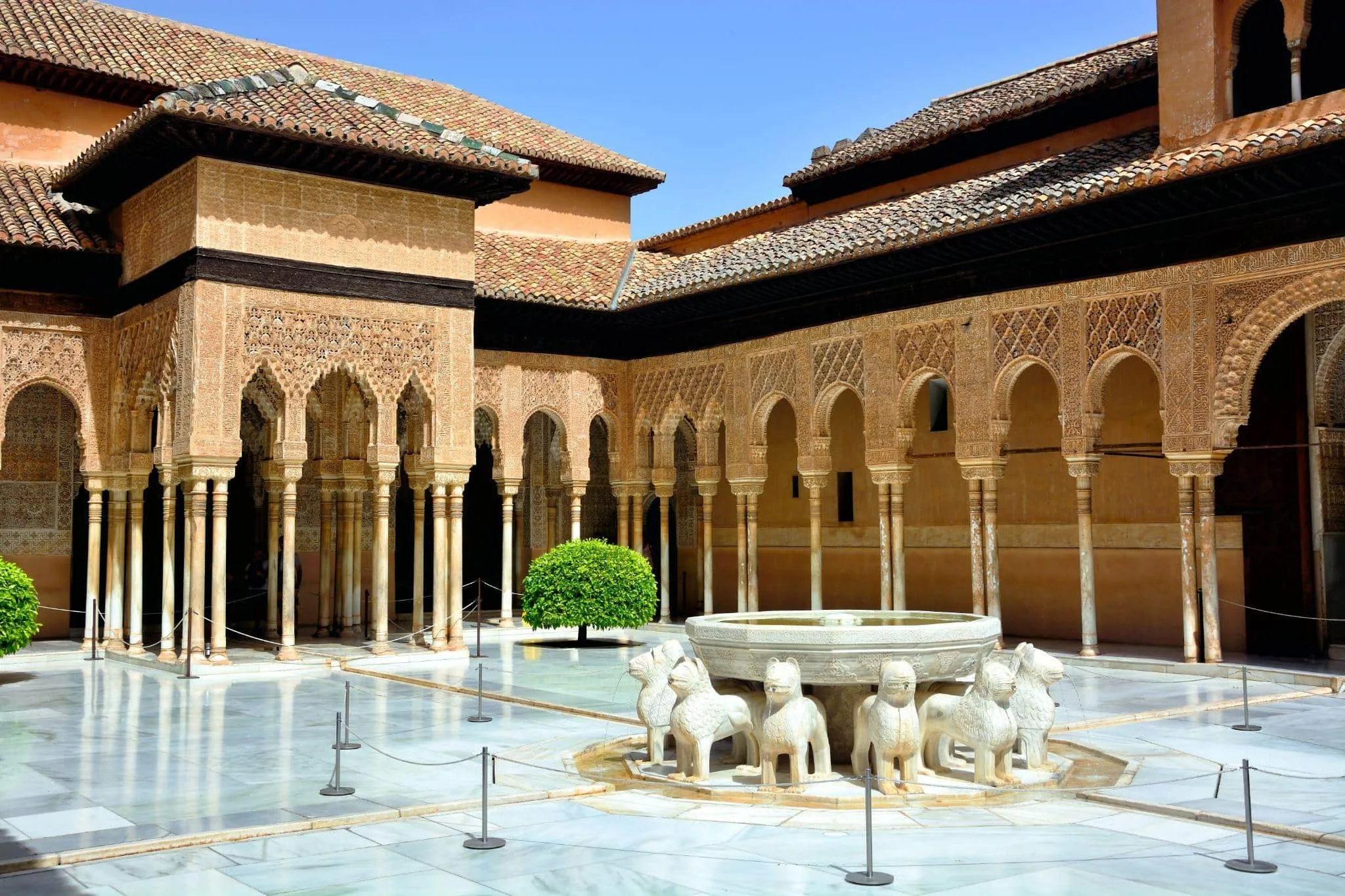 The Court of the Lions in the Alhambra: a fountain borne by stone lions in a marble courtyard, ringed by slender columns and carved arcades under tiled roofs