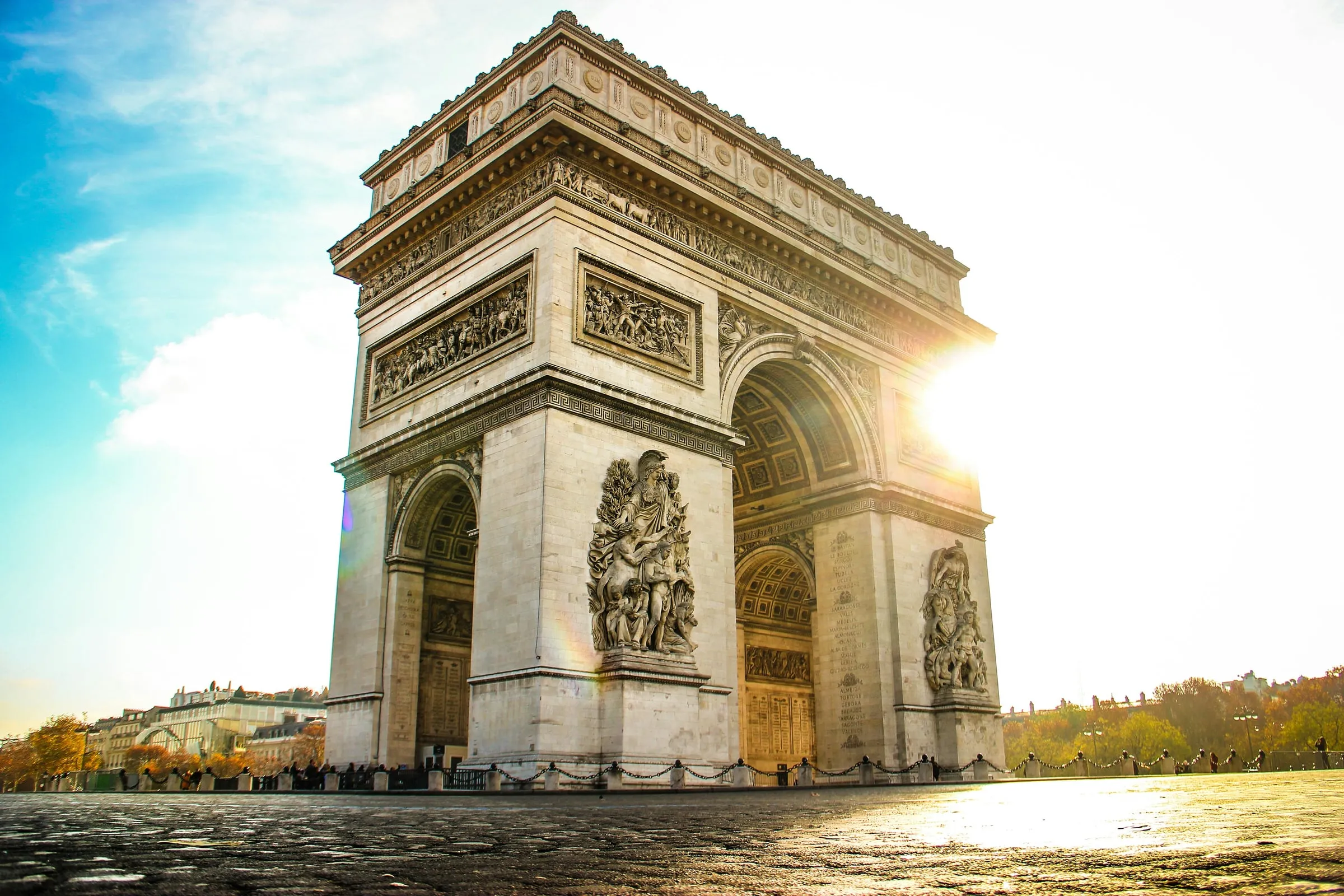 The Arc de Triomphe from the cobbles of the Place Charles-de-Gaulle, the low morning sun flaring through its arch and lighting the sculpted reliefs on its piers