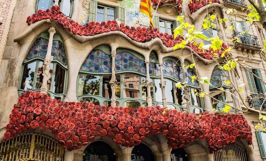 Casa Batlló's undulating façade with its stained-glass windows, the stone balconies and window ledges heaped with red roses, a Catalan flag above and new spring leaves on a tree in front