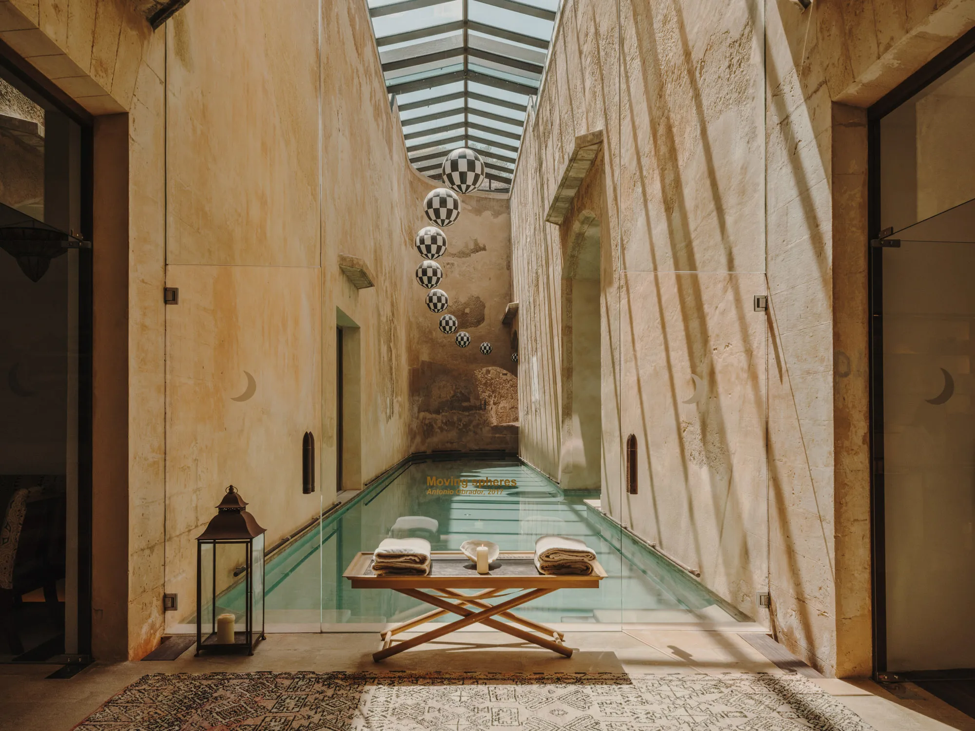 The spa's saltwater pool: a long narrow pool between high bare stone walls under a pitched glass roof, with a line of black-and-white chequered spheres hanging above it and a folding table of rolled towels at the near end