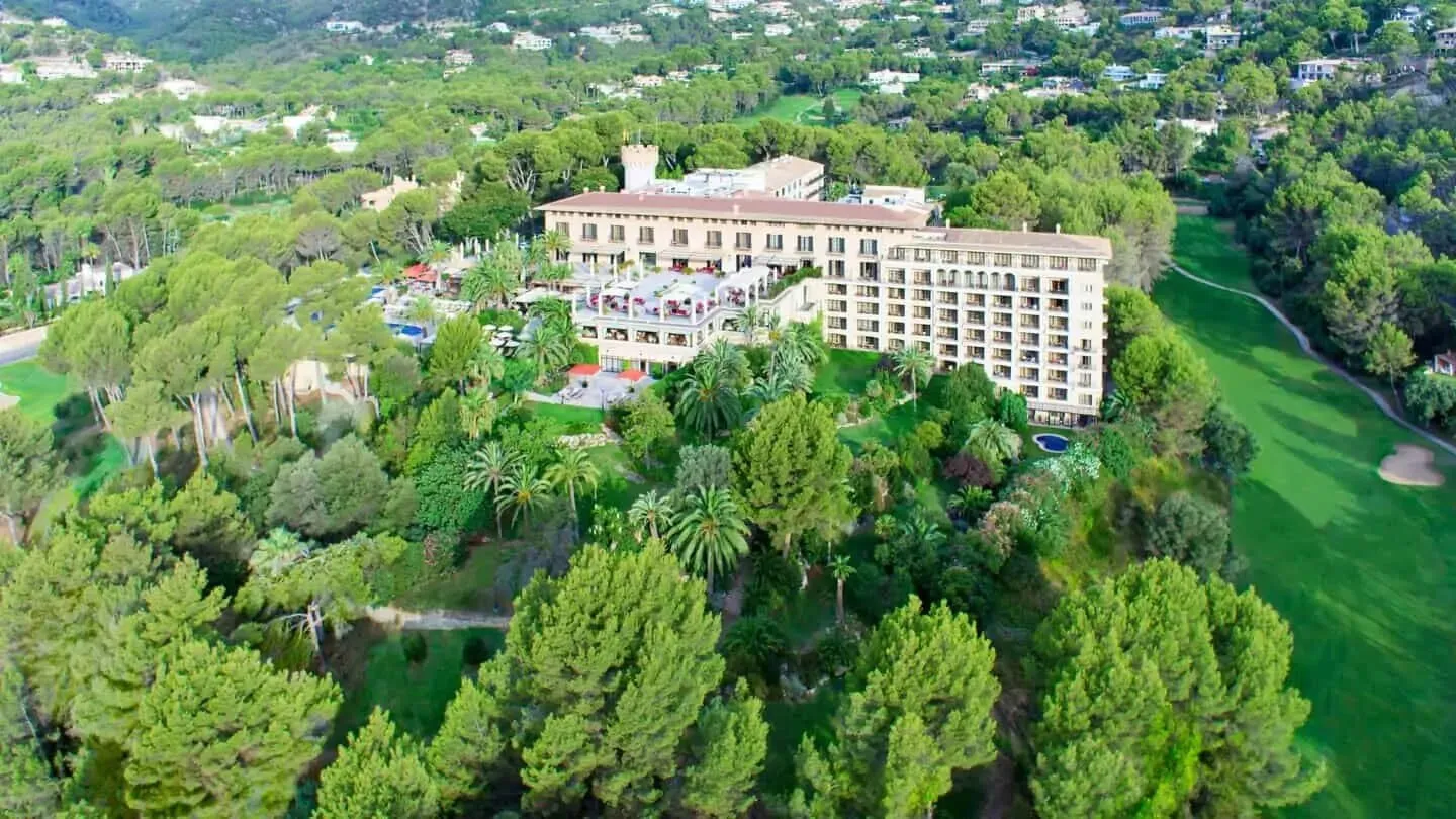 Castillo Hotel Son Vida from the air, its tower and long wings set in pine woods beside a golf fairway, with villas on the hillside behind