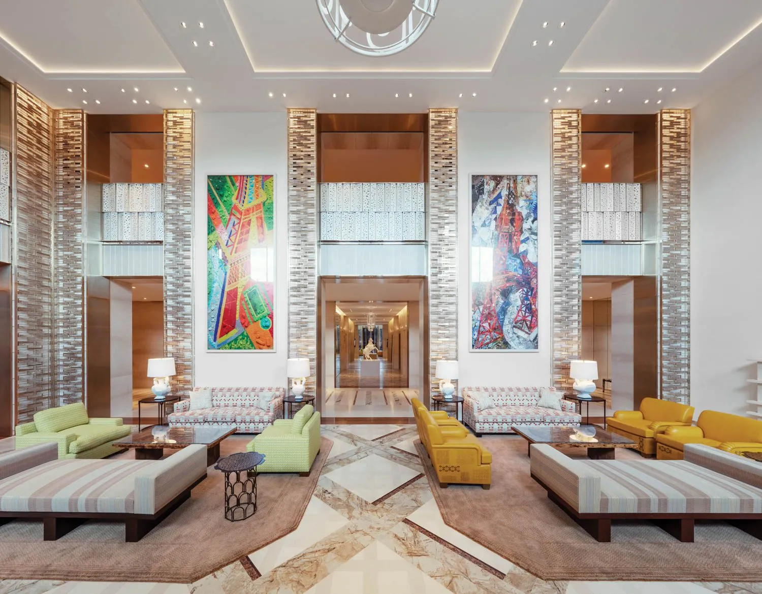 A double-height lobby with glass-brick pillars and two tall, brightly coloured paintings of the Eiffel Tower, sofas and armchairs in green, yellow and patterned fabric on a marble floor laid in diamonds, and a corridor leading away at the centre