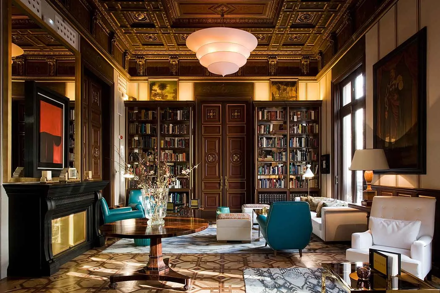 The library at Cotton House, with glass-fronted bookcases, a gilded coffered ceiling and teal armchairs