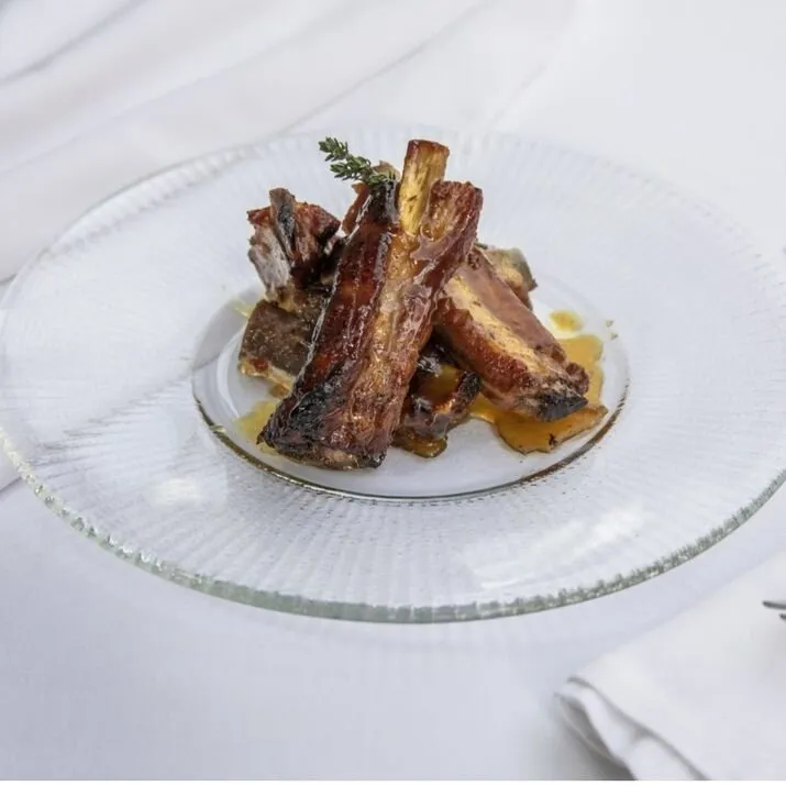 Glazed pork ribs with a sprig of thyme on a ribbed glass plate, set on a white tablecloth