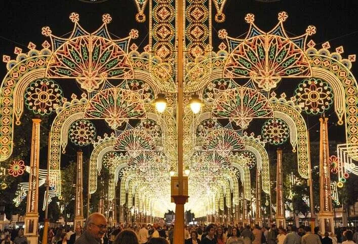 Arches of festival lights glowing gold, green and red over a crowded avenue at night, receding into a long tunnel of light