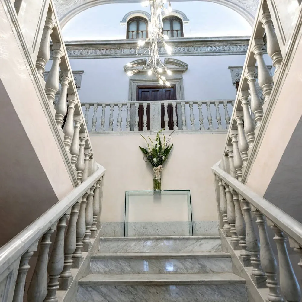 The palace's white marble staircase, its balustrades rising either side to a gallery under a chandelier of bare bulbs