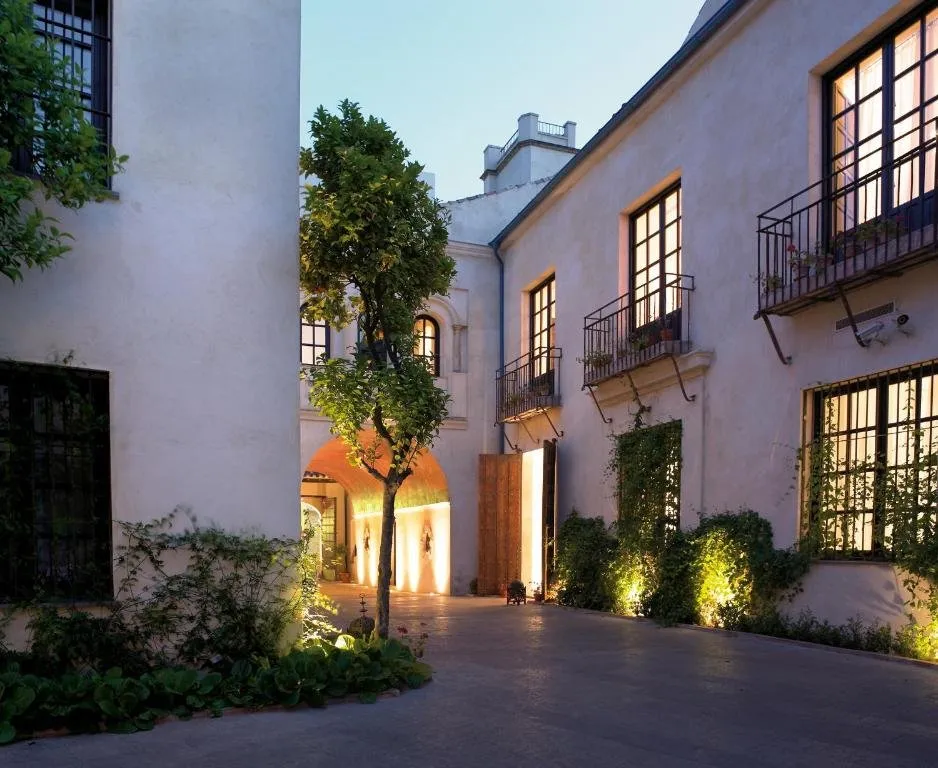 A courtyard of the palace at dusk: an orange tree before a lit arched passage, between white walls with iron balconies