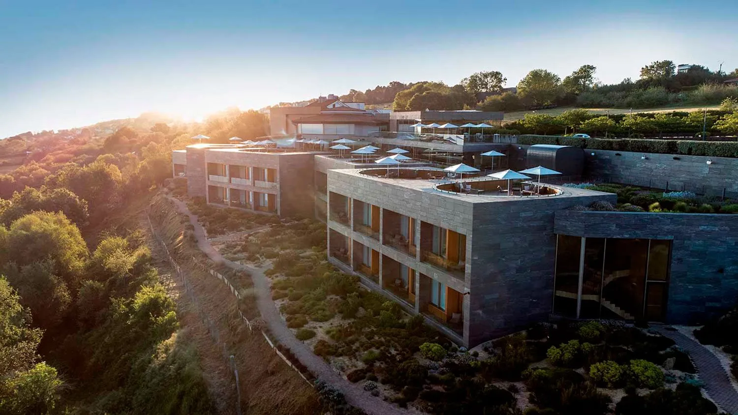 Hotel Akelarre from the air: slate-clad wings stepped down a green hillside, with parasols on the roof terraces