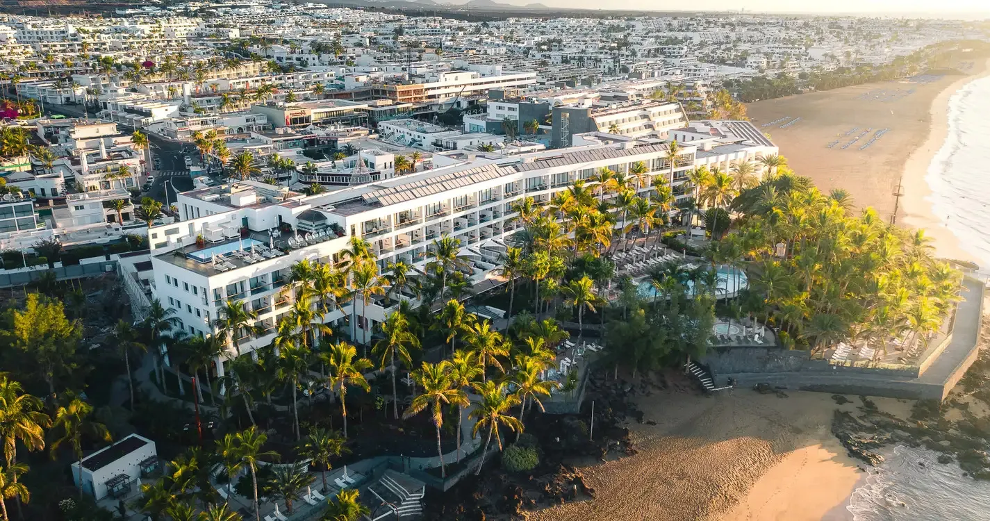 Hotel Fariones from the air at sunset: a long white building among palms, with a pool below it and the beach and sea to one side