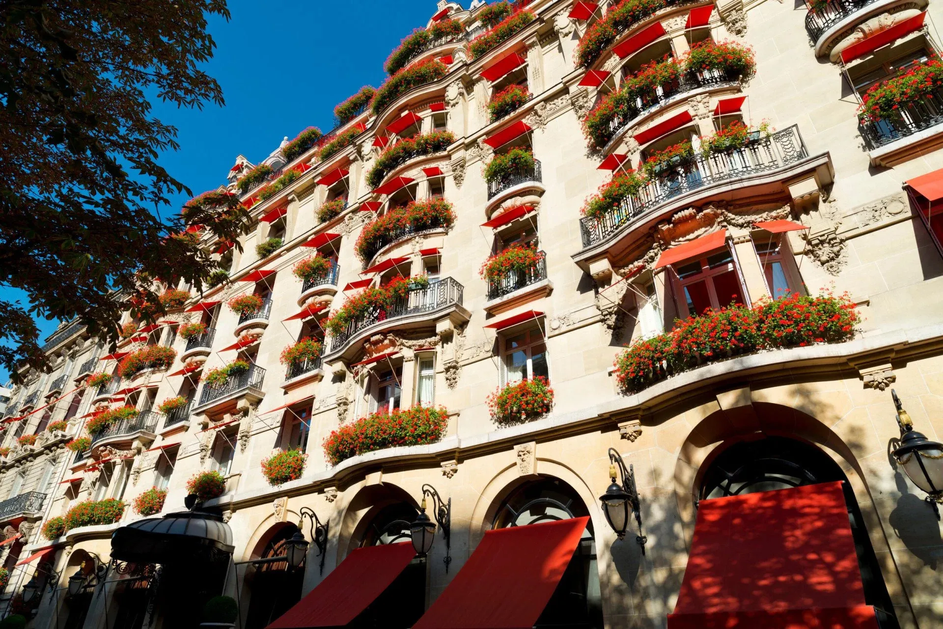 The hotel's stone façade, its balconies spilling red geraniums under red awnings, against a deep blue sky
