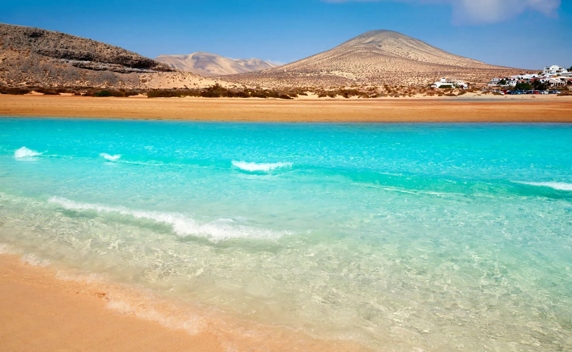 A shallow turquoise lagoon at Jandía on Fuerteventura, with pale sand and low volcanic hills behind