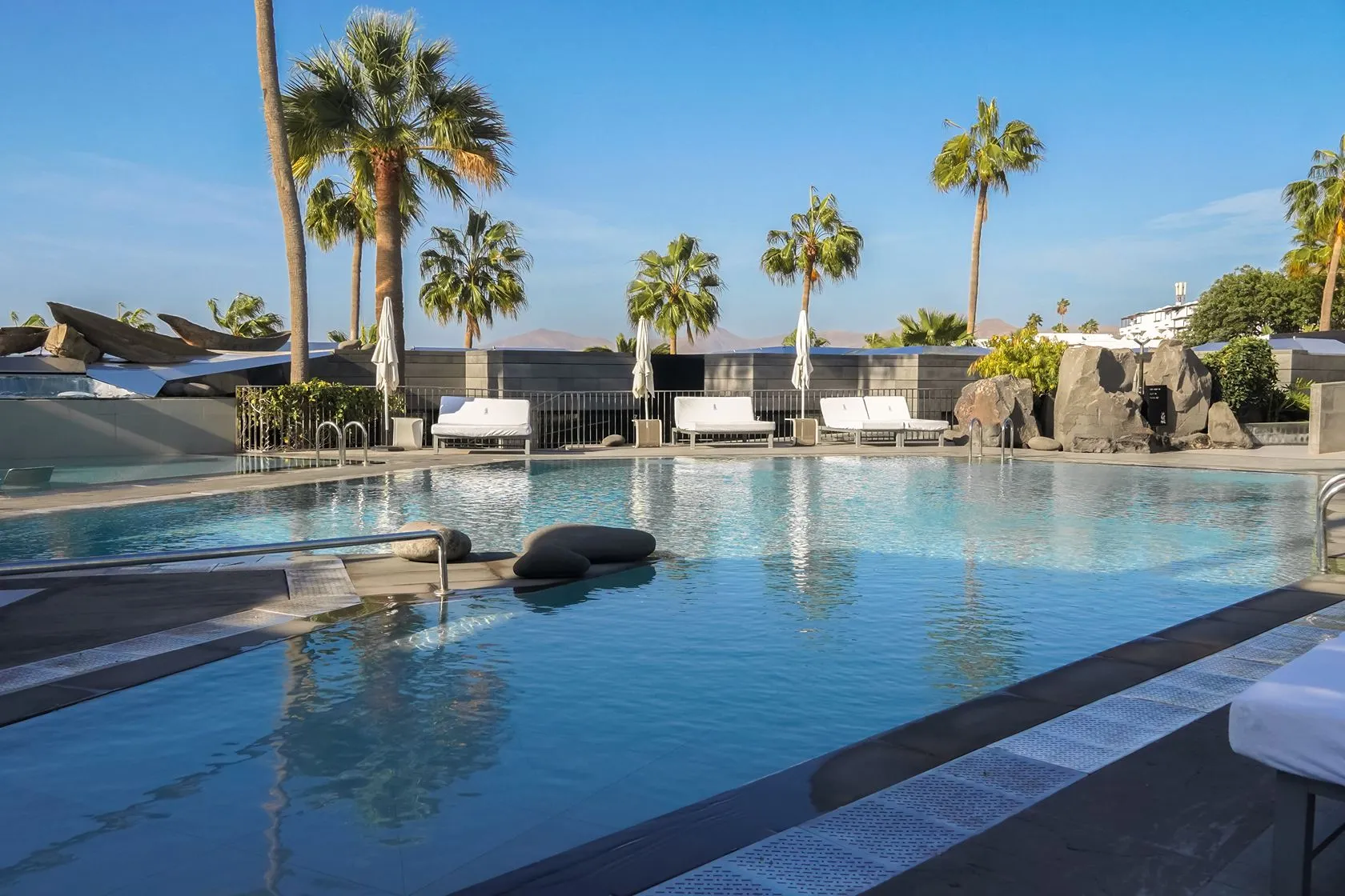 The pool at La Isla y el Mar in the morning, with palms, day beds and dark volcanic boulders along its edge