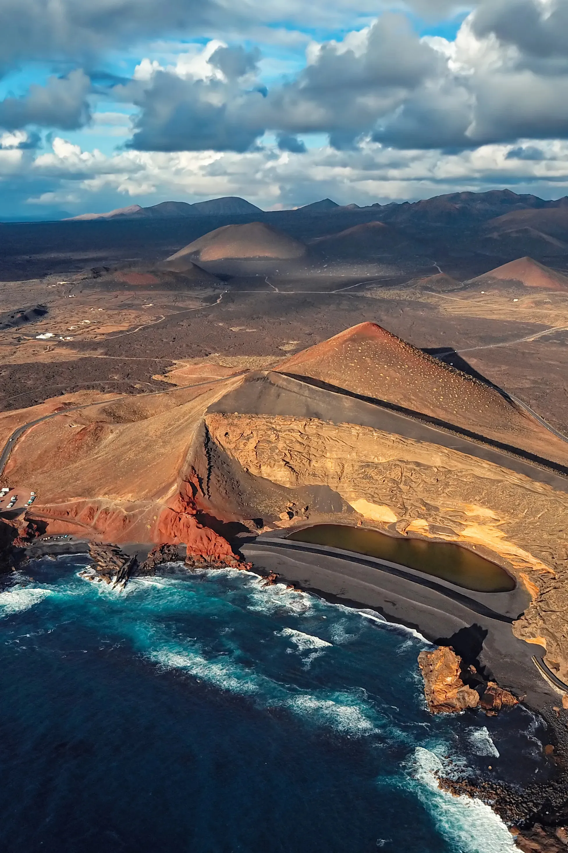 El Golfo from the air: a green lagoon behind a black beach in a half-eroded crater, with volcanic cones inland