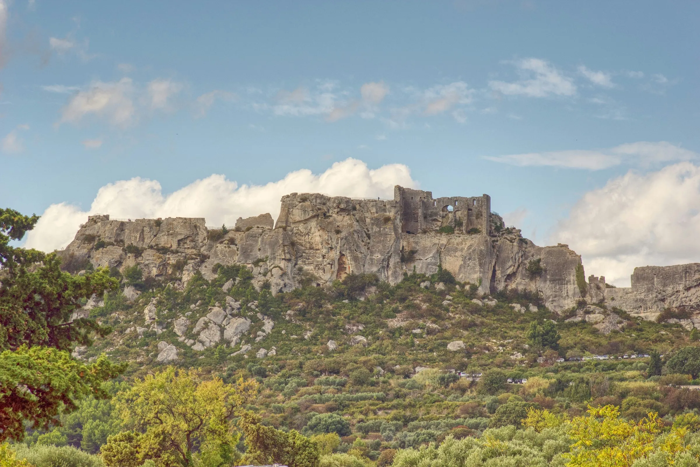 Les Baux-de-Provence from the valley: the ruined keep and walls of the castle along the crest of the white limestone rock, the village's houses below it and olive trees in the foreground