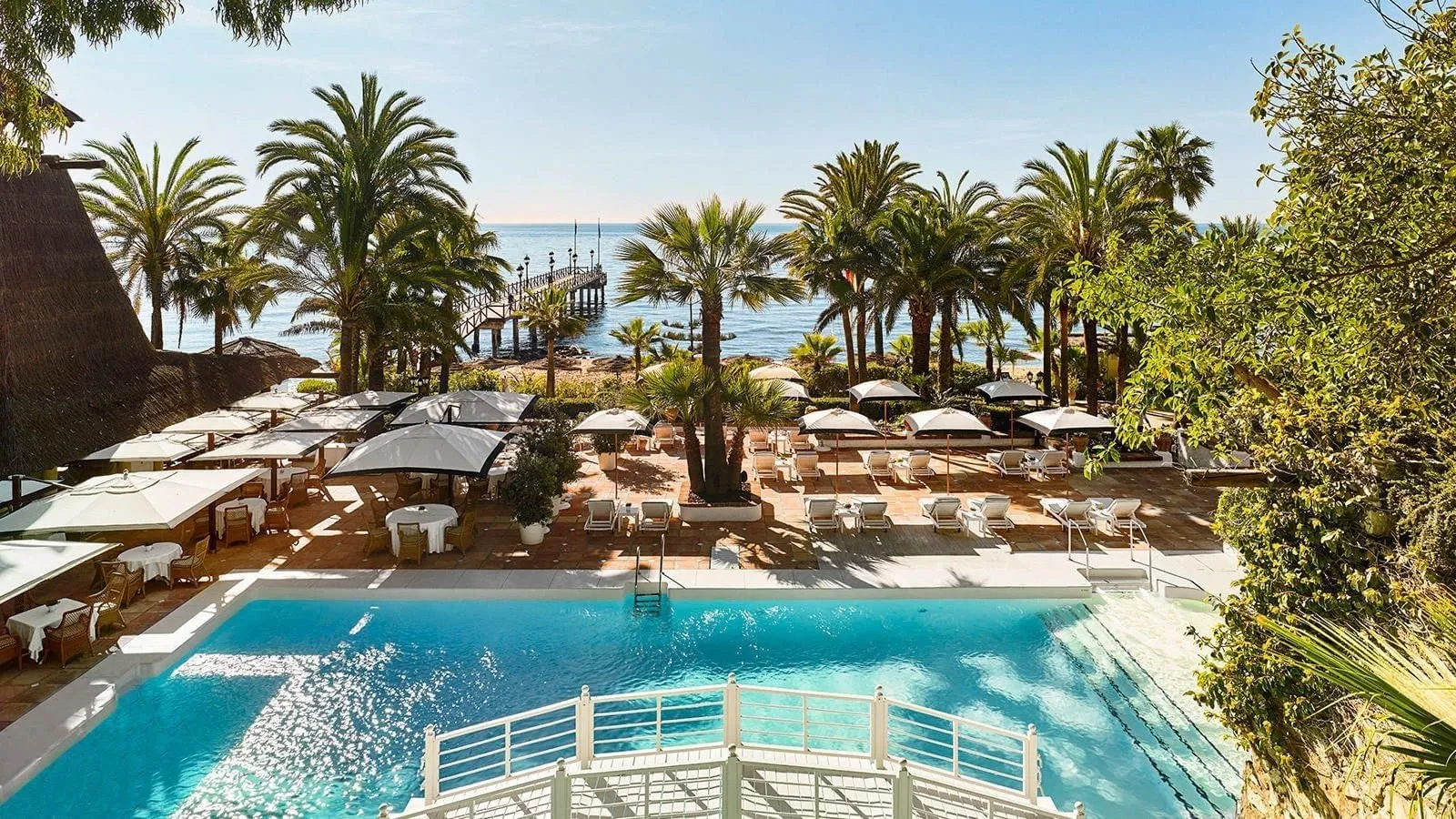 The Beach Club pool at Marbella Club, with palms, white parasols and a wooden pier running out to sea