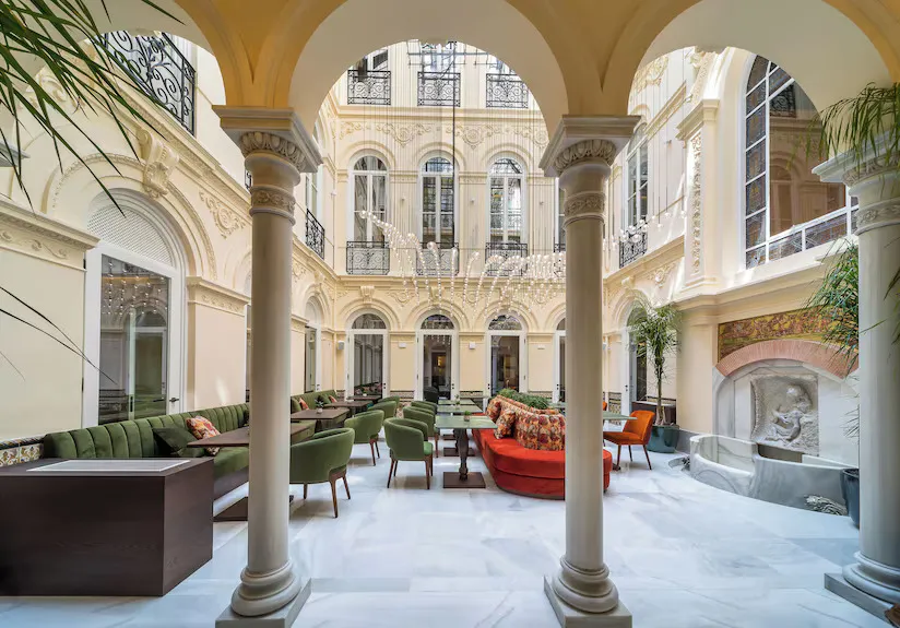 El Patio, the hotel's restaurant in its arcaded courtyard: green velvet seats and a red sofa among the tables, under tall windows and iron balconies