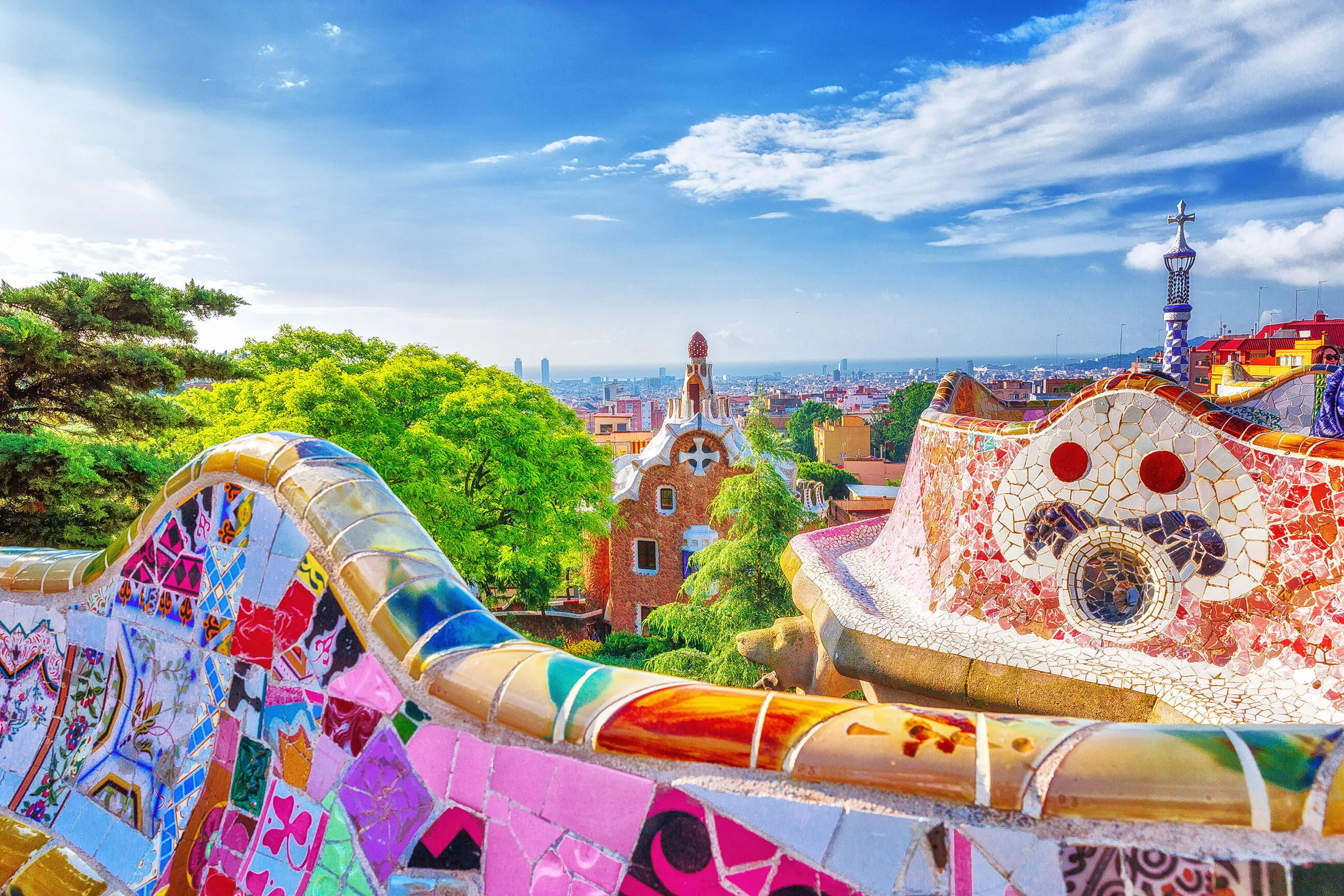 The trencadís mosaic of Park Güell in the foreground, one of Gaudí's gatehouses below and Barcelona running down to the sea