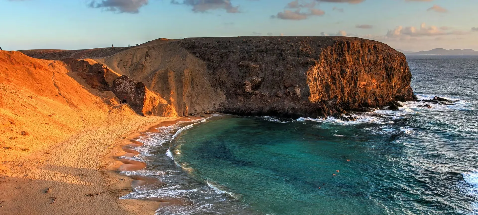 A cove at Playa de Papagayo at sunset, pale sand between ochre cliffs and clear green water
