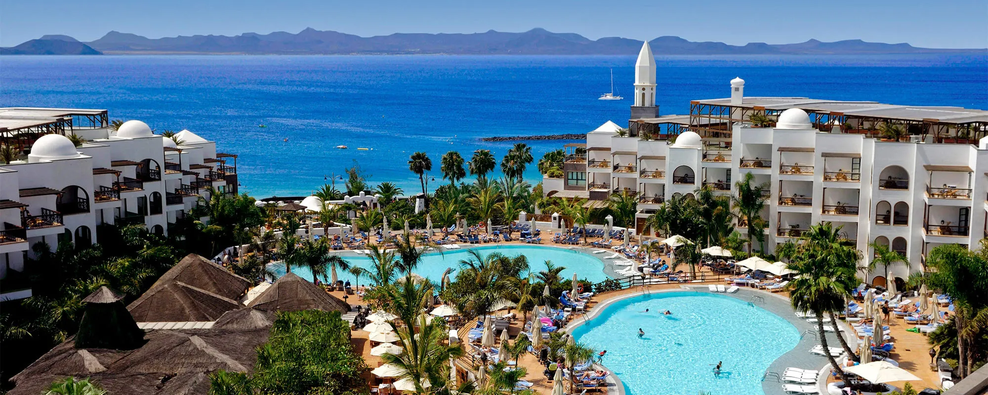 Princesa Yaiza from above: white domed buildings around two curving pools and palms, with the beach and the blue strait beyond