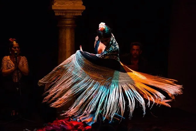 A flamenco dancer spinning a long fringed shawl, with a singer at a microphone and a seated musician behind her