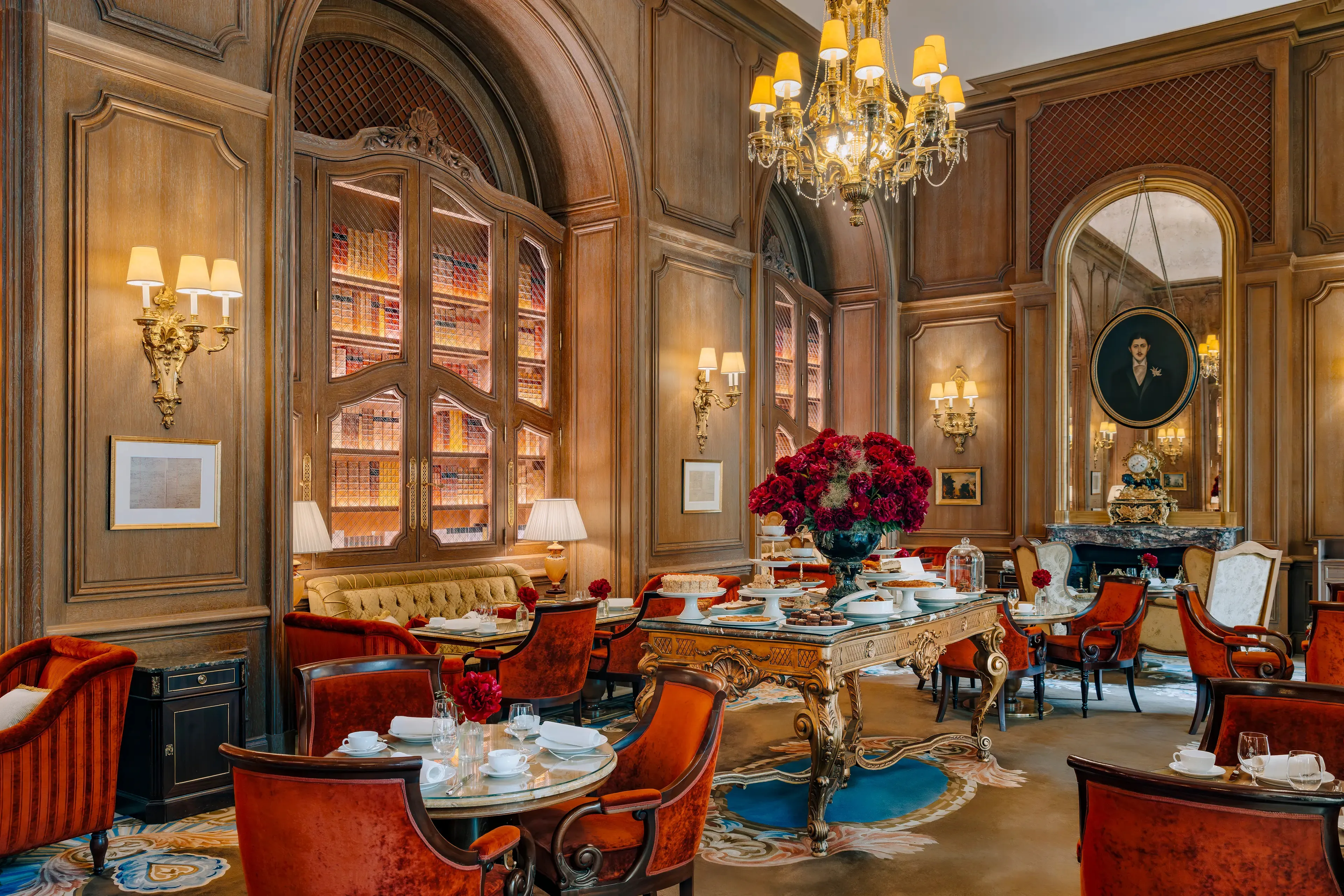 The Salon Proust at the Ritz Paris: panelled walls, glass-fronted bookcases, orange velvet armchairs and a table of cakes for tea