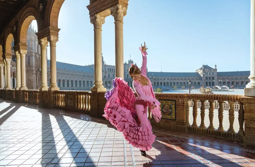 A flamenco dancer mid-turn in the Plaza de España in Seville, her skirt spread, the brick arcade behind her