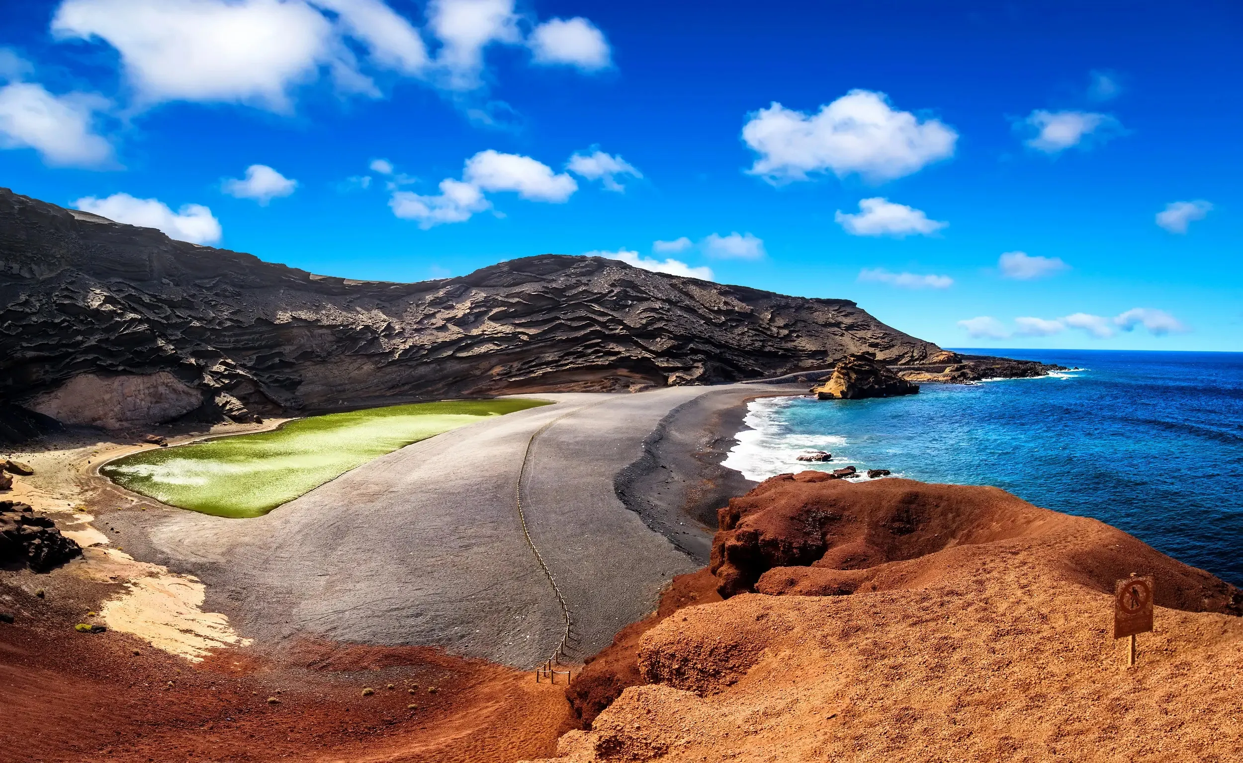 The green lagoon of Charco de los Clicos at El Golfo, behind a black beach under a half-eroded crater wall