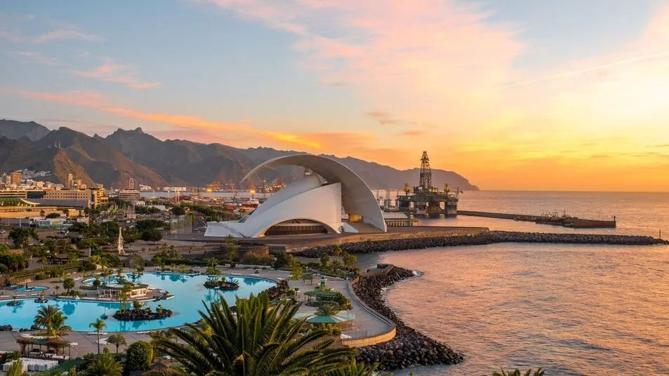 Santa Cruz de Tenerife at sunset: the white curved shell of the Auditorio on the waterfront, the sea pools of the Parque Marítimo in front and the Anaga hills behind