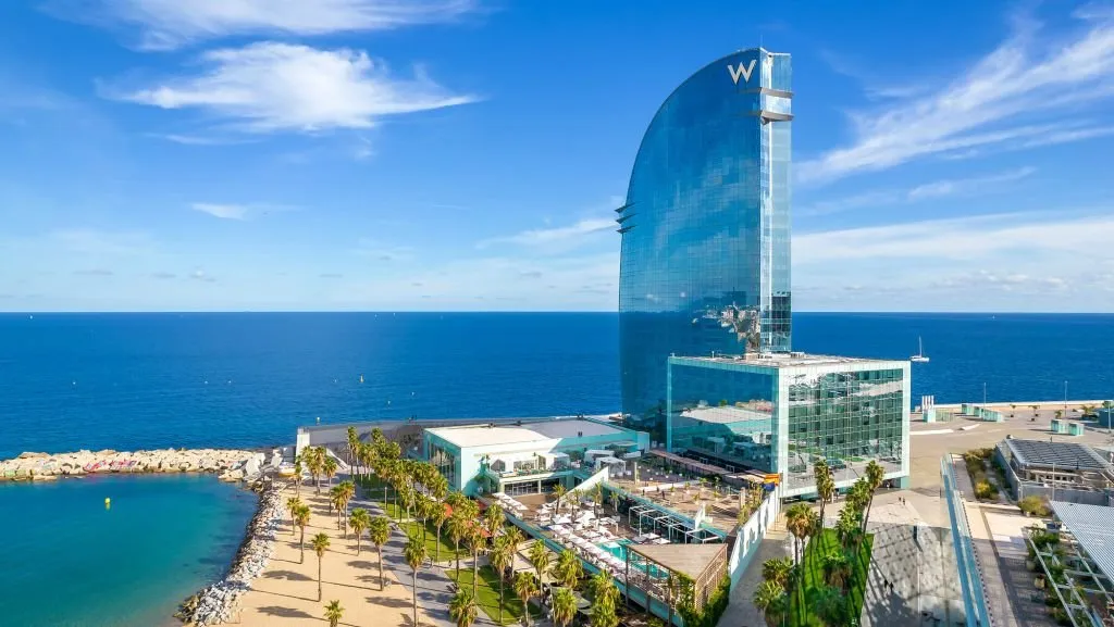 W Barcelona's sail-shaped glass tower by the sea, with its pool terraces and a palm-lined beach below
