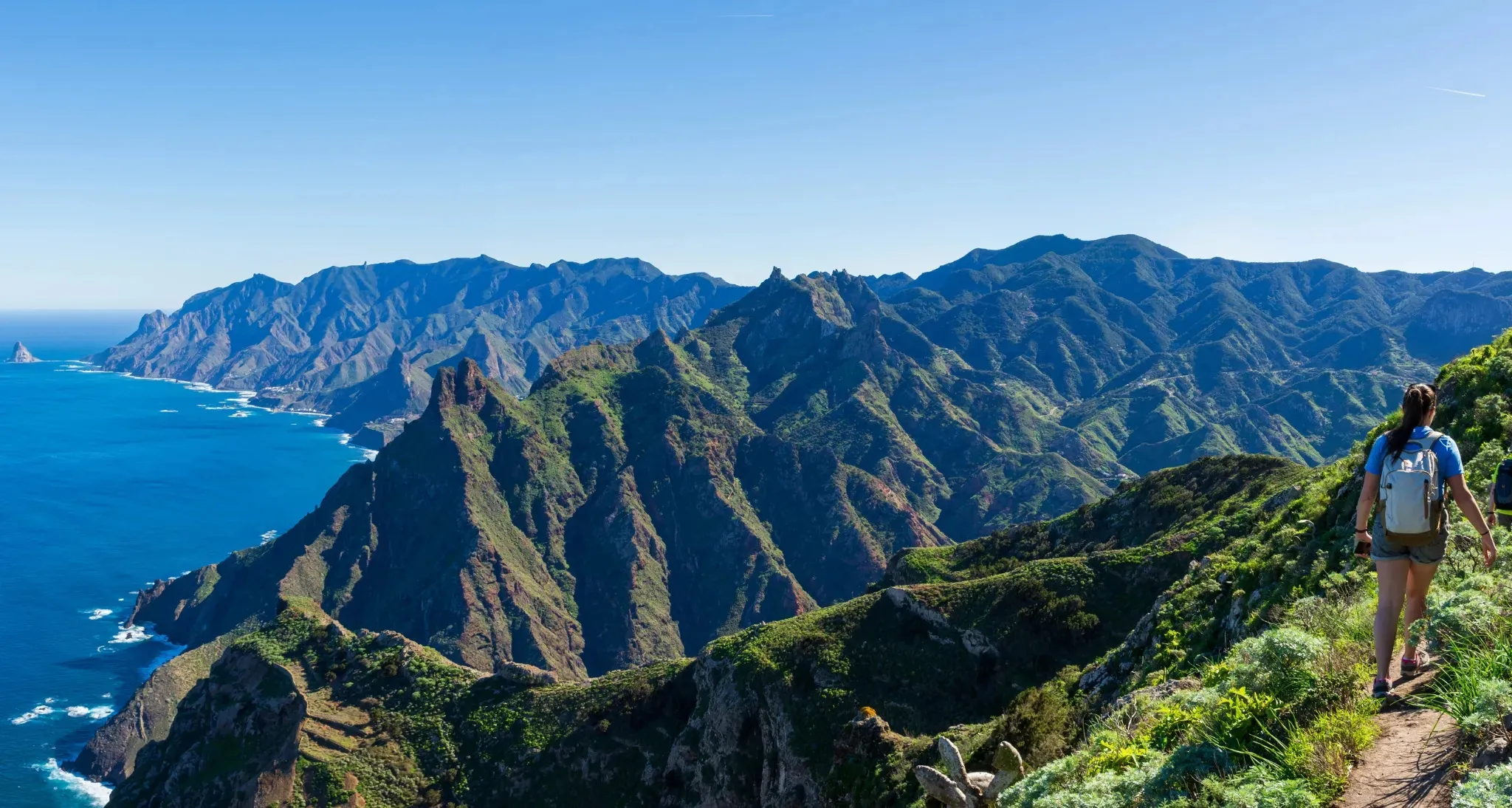A walker on a ridge path in the Anaga massif, with green ridges falling to the Atlantic
